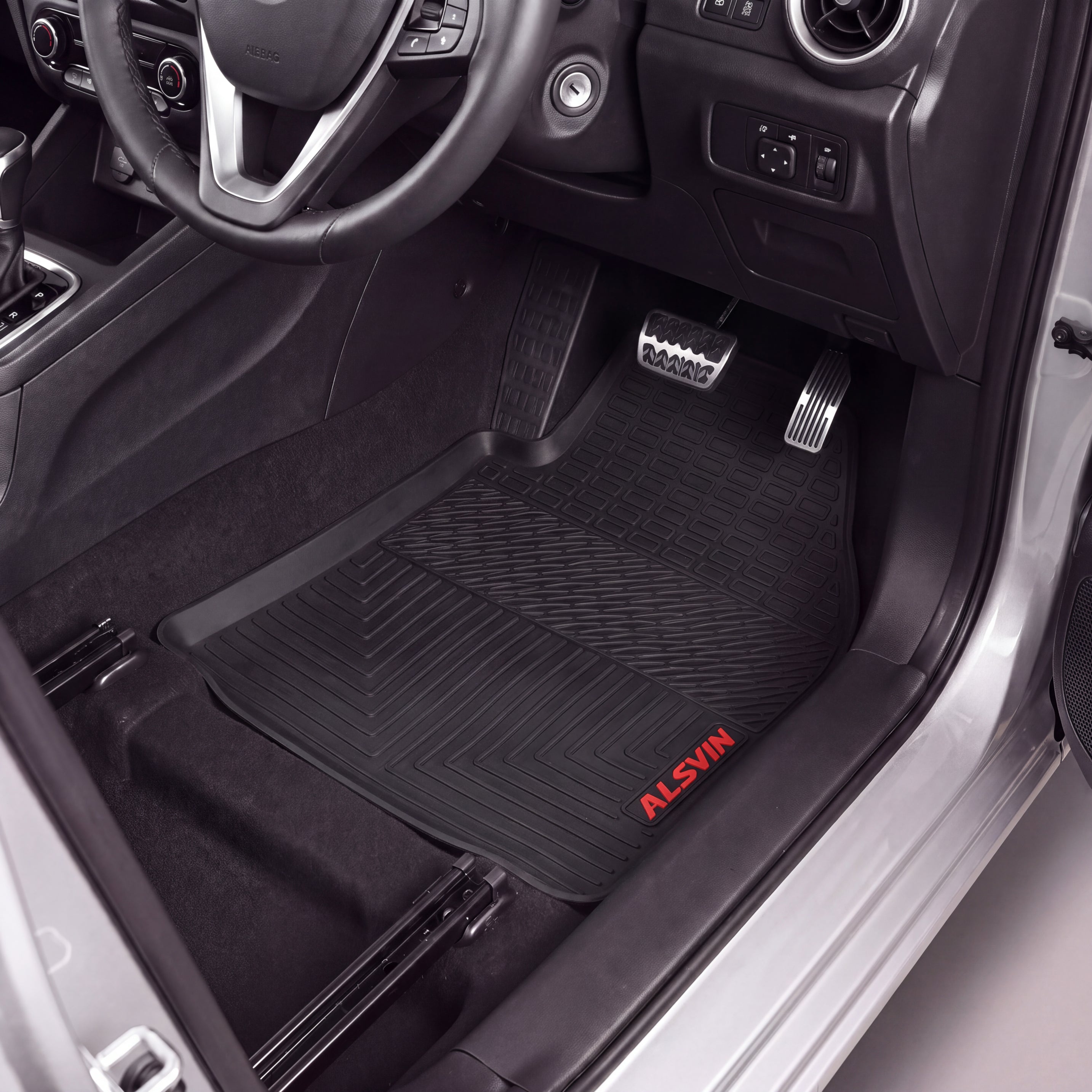 Black Alsin floor mats installed in a car's driver's side footwell, shown with the door open and interior visible.
