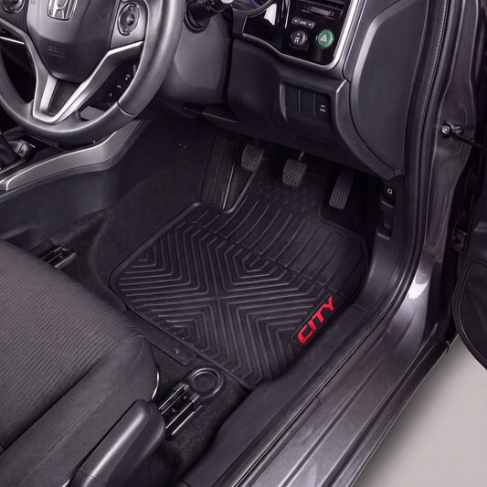 A black rubber car floor mat with a textured geometric pattern and a red 'CITY' logo, shown installed in the driver's footwell of a vehicle interior.