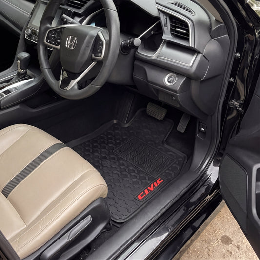 Black car floor mats with red 'CIVIC' branding installed in a Honda Civic driver's seat, shown with the door open and the interior dashboard and beige seats visible.