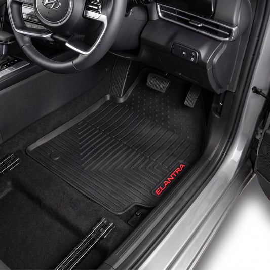 Black rubber car floor mats installed in the front footwells of a Hyundai Elantra, with the red 'ELANTRA' logo printed on the passenger side mat.