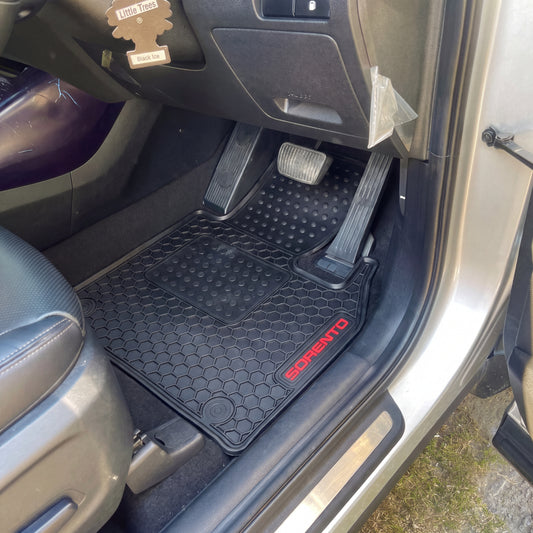 Black textured car floor mats with red 'SORENTO' branding, shown installed inside a vehicle door with the door open.