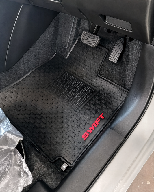 Black car floor mat with a diamond-plate pattern and red 'SWIFT' lettering, installed inside a vehicle door.