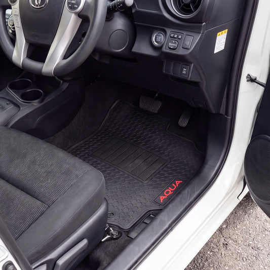 Black car floor mats installed in the front passenger and driver footwells of a white vehicle, with red 'AQUA' branding on the passenger mat.