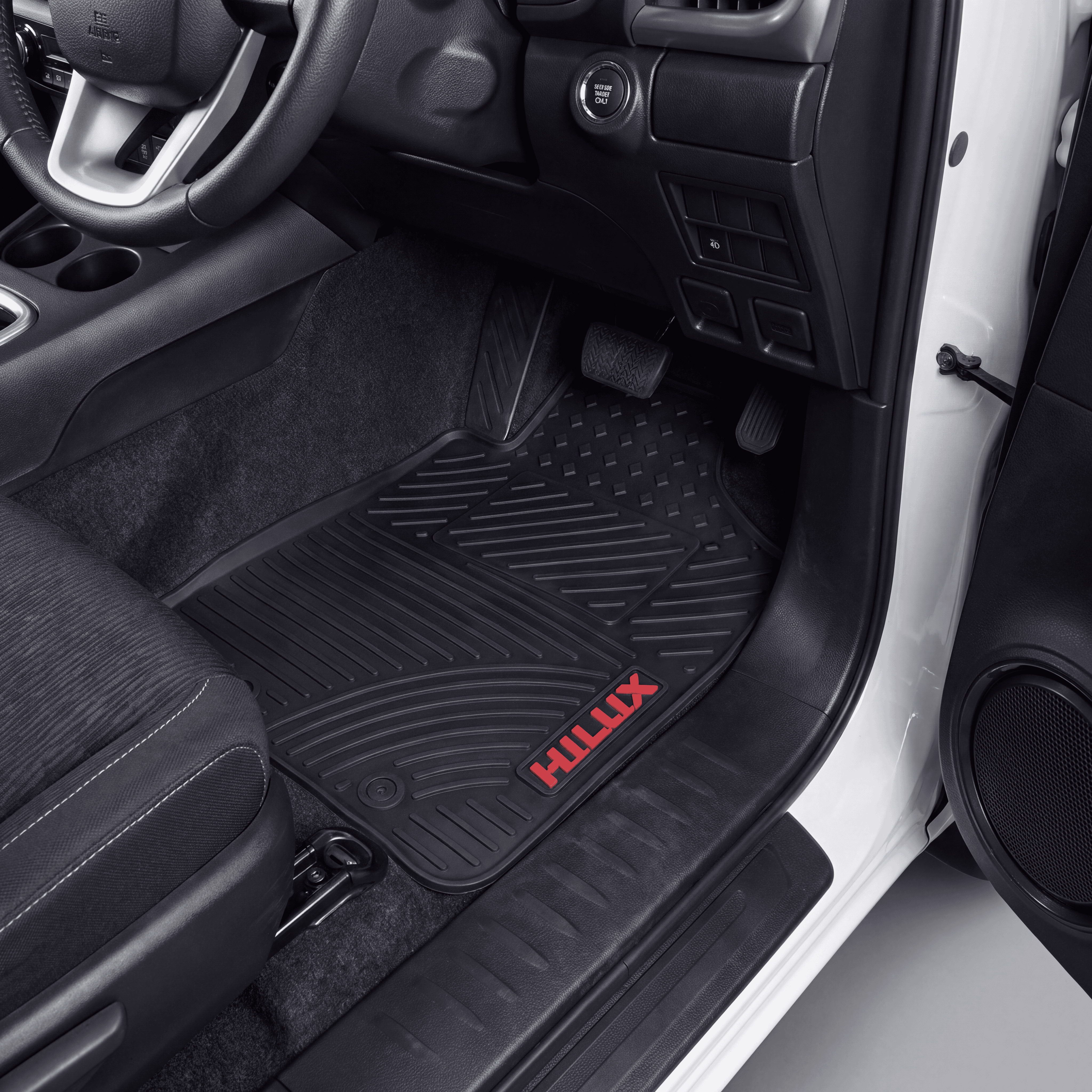 Black rubber car floor mat with a red HILUX logo, shown installed in the driver's footwell of a vehicle interior.