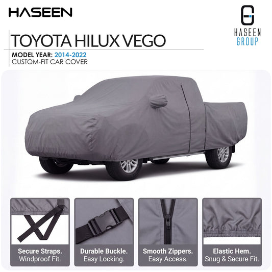A gray car cover fitted over a Toyota Hilux Vego pickup truck, shown on a white background with Haseen branding and feature callouts for straps, buckle, zippers, and hem.
