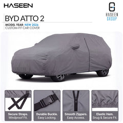 A gray car cover fitted over a car, shown on a white background with HASEEN branding and feature callouts. The image includes text reading 'BYD ATTO 3', 'MODEL YEAR: NEW 2026', and four small inset detail panels at the bottom highlighting straps, buckle, zippers, and hem.