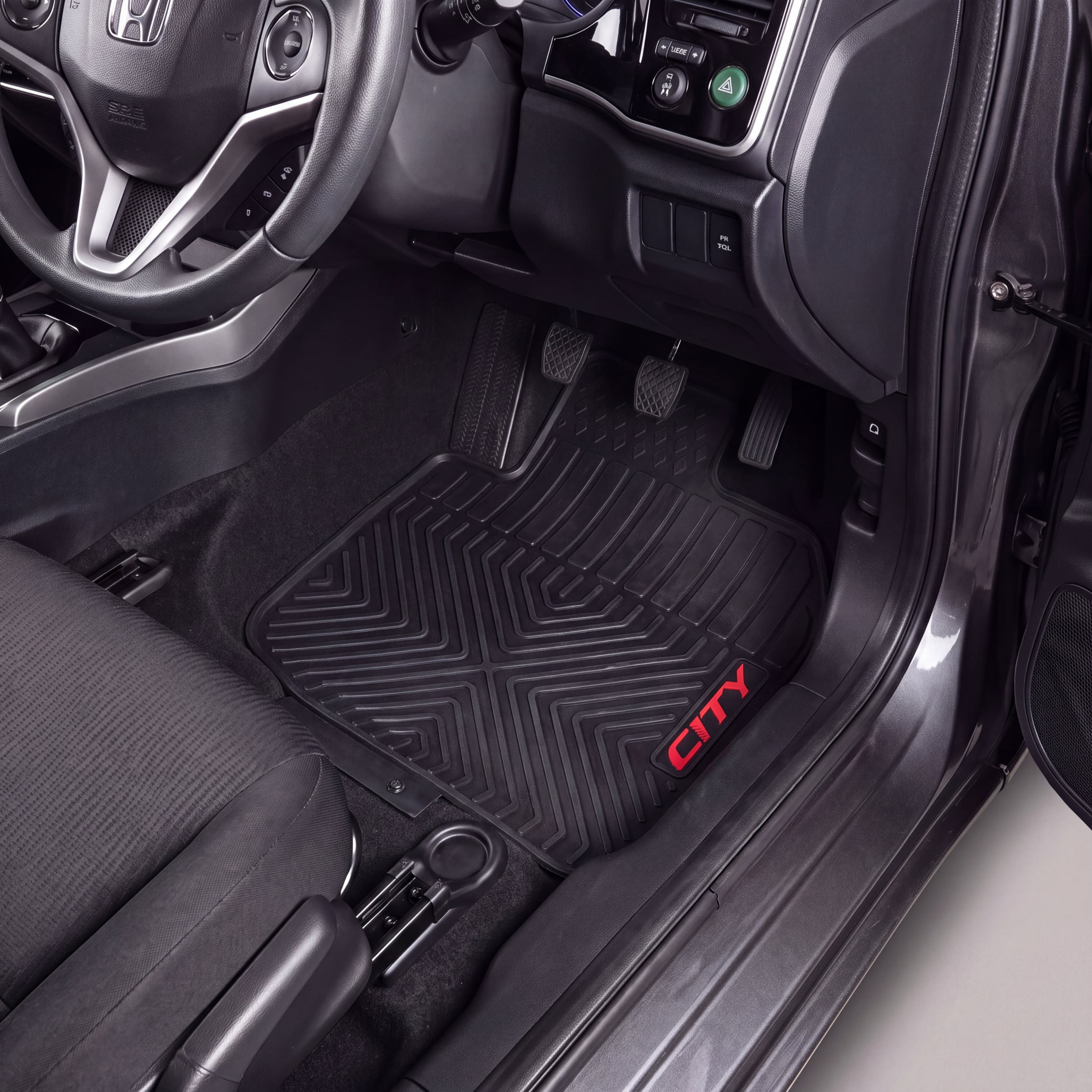 A black rubber car floor mat with a textured geometric pattern and a red 'CITY' logo, shown installed in the driver's footwell of a vehicle interior.
