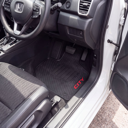 Black car floor mat with a diamond-embossed pattern and red 'CITY' text, shown installed inside a white vehicle near the open driver's side door.