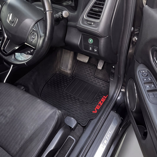 Black rubber car floor mats with red 'VEZEL' branding, shown installed inside a Honda Vezel vehicle.