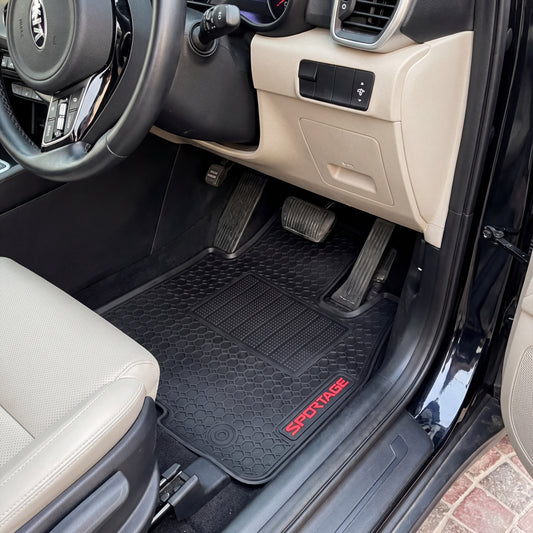 A pair of black textured car floor mats installed in the front cabin of a vehicle with beige seats. The driver's side mat features the brand name 'SPORTAGE' in red text near the bottom.