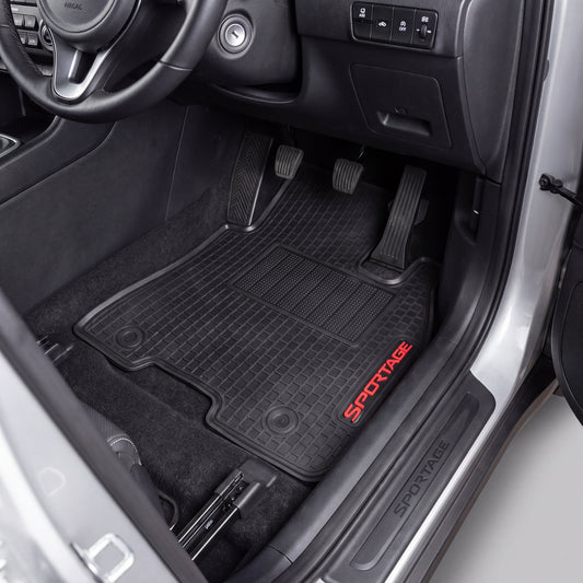 Black car floor mats with red SPORTAGE lettering, shown installed inside a vehicle's footwell next to the open door.