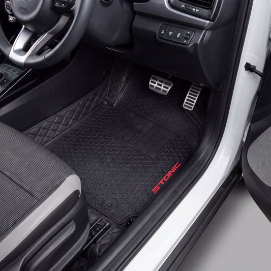 Black car floor mats installed in a vehicle's footwell, with a diamond-quilted pattern and a red STONIC logo embroidered on the side, shown from the open driver's side door.