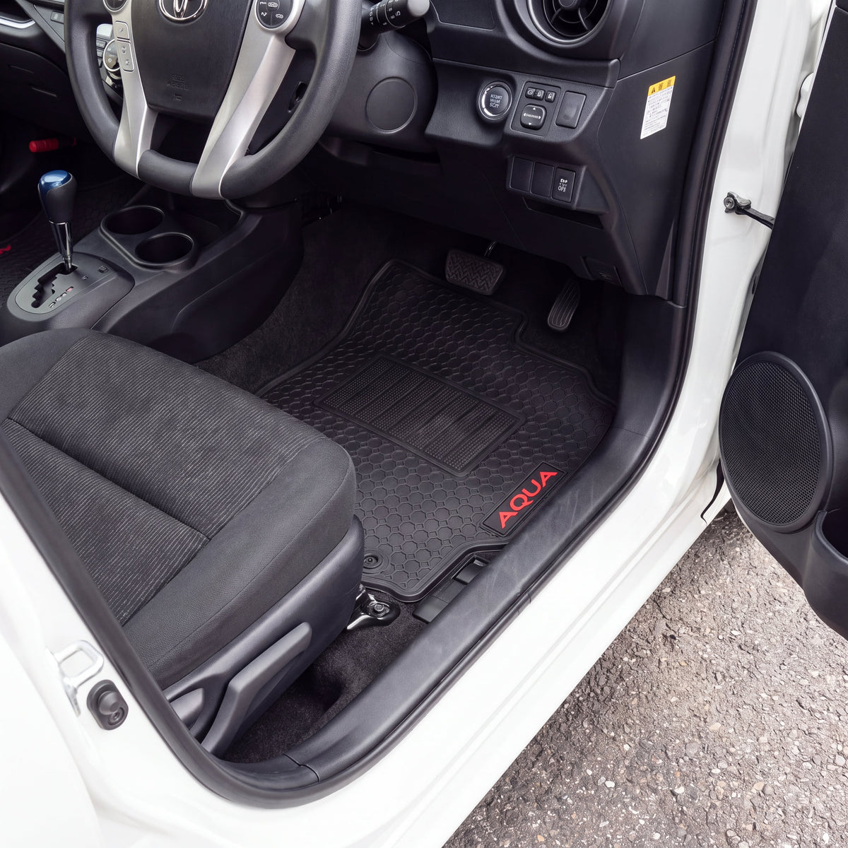 Black car floor mats installed in the front passenger and driver footwells of a white vehicle, with red 'AQUA' branding on the passenger mat.