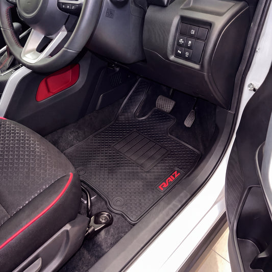 Black rubber car floor mats with red 'RAIZ' branding, installed in the driver's side of a vehicle interior.