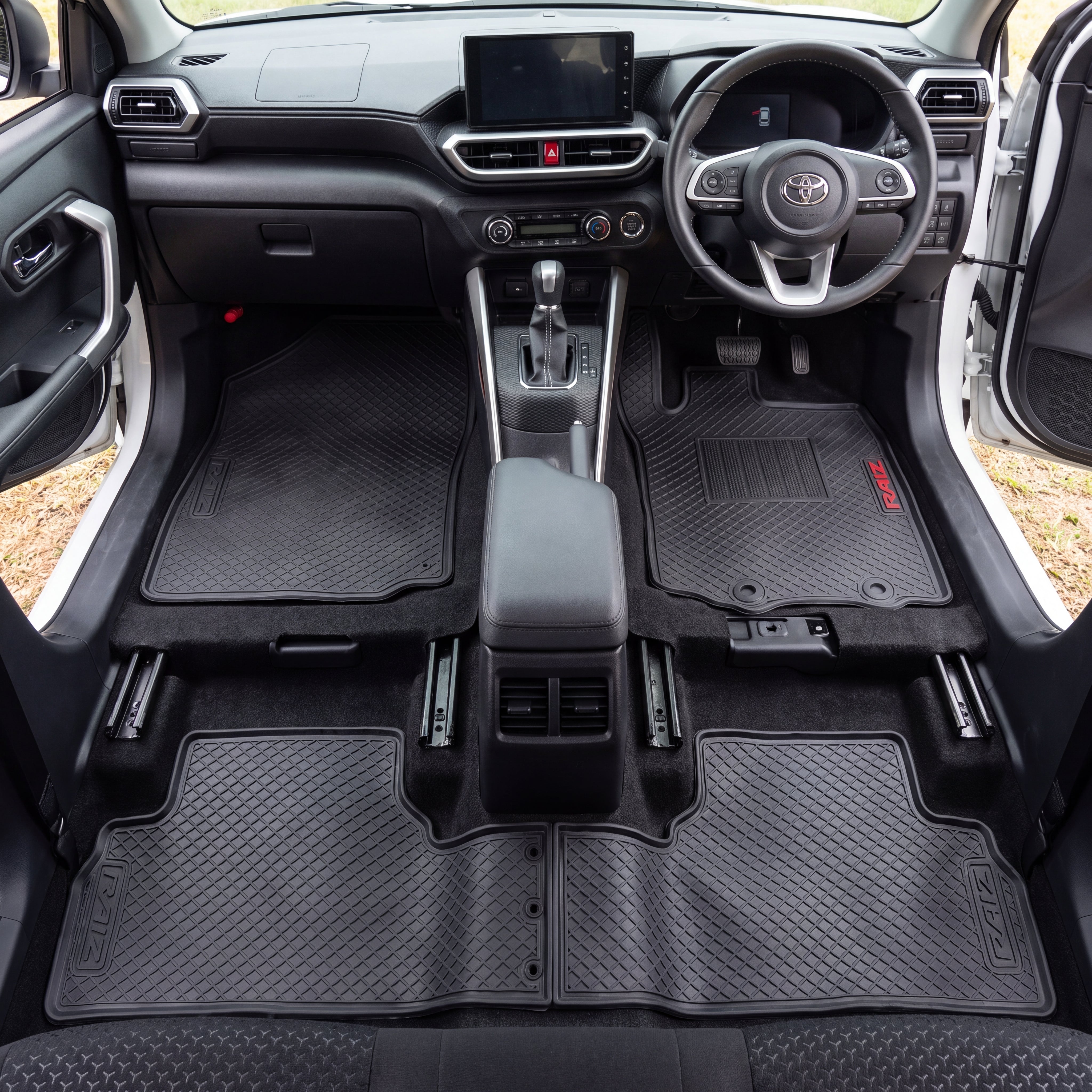 A set of black textured car floor mats installed in the front and rear of a vehicle interior, shown from a top-down view. The mats are fitted around the footwells and center console area, with the Toyota emblem visible on the steering wheel.