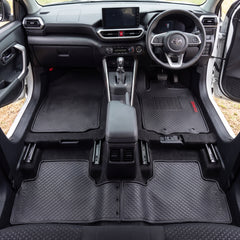 A set of black textured car floor mats installed in the front and rear of a vehicle interior, shown from a top-down view. The mats are fitted around the footwells and center console area, with the Toyota emblem visible on the steering wheel.