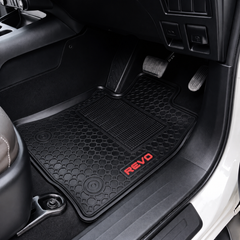 Black textured rubber car floor mat with a red REVO logo, shown installed in a vehicle's footwell.